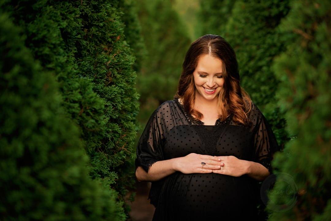 pregnant woman in black dress standing next to trees.  iris lane photography akron canton green hartville ne ohio
