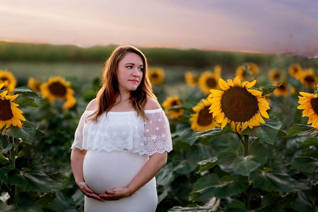 pregnant woman in white dress standing in sunflower field.  iris lane photography akron canton green hartville ne ohio