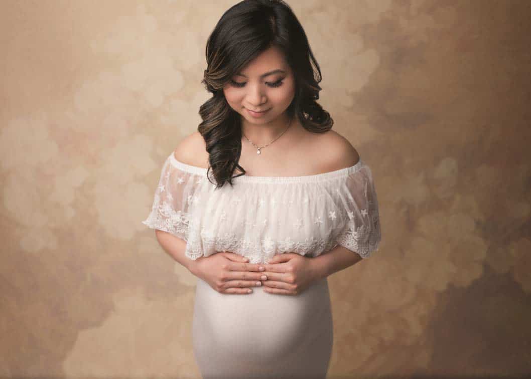 Pregnant woman in white lace dress hands on belly studio maternity photo. Iris Lane Photography NE Ohio maternity photographer